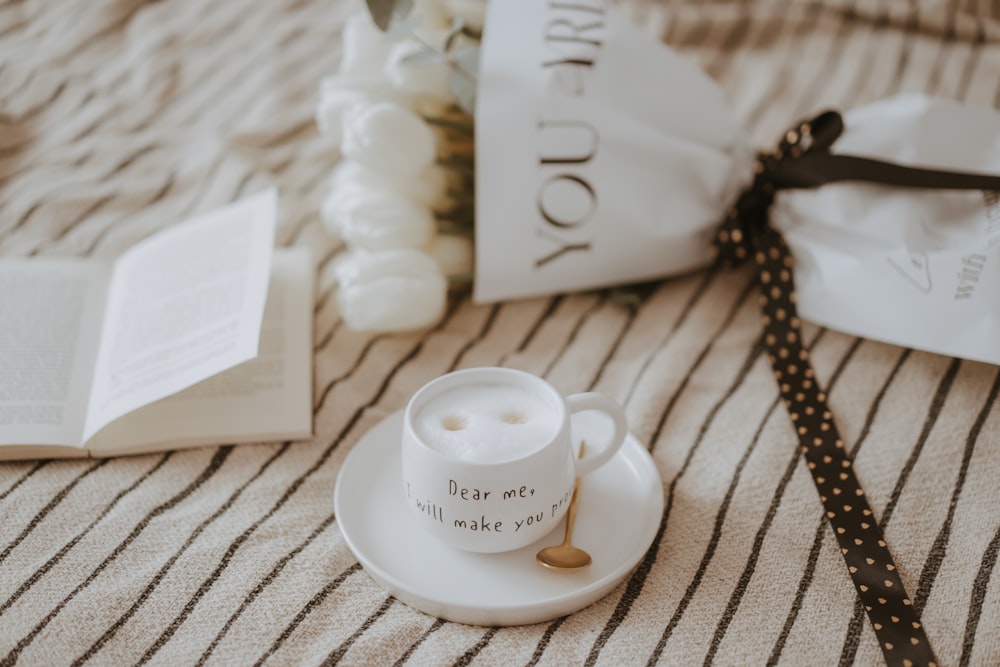 a cup and saucer on a bed next to a book
