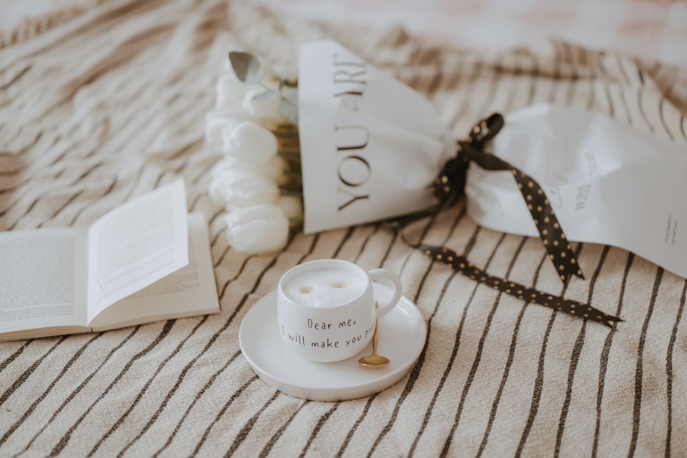 a coffee cup sitting on top of a bed next to a book