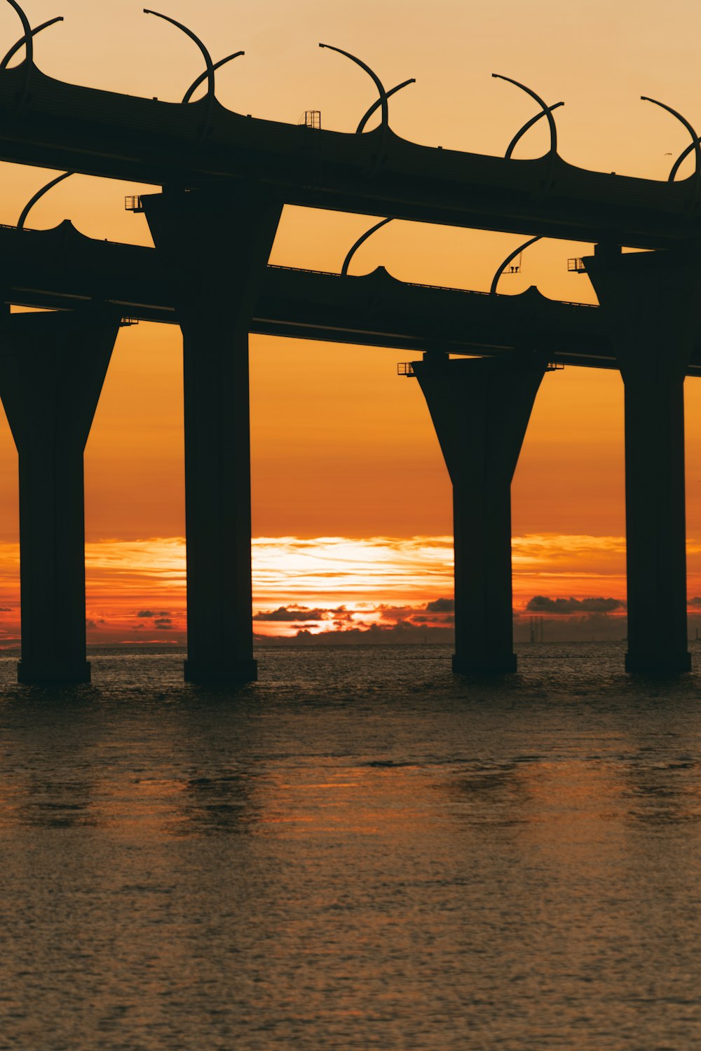 the sun is setting over the ocean with a bridge in the background