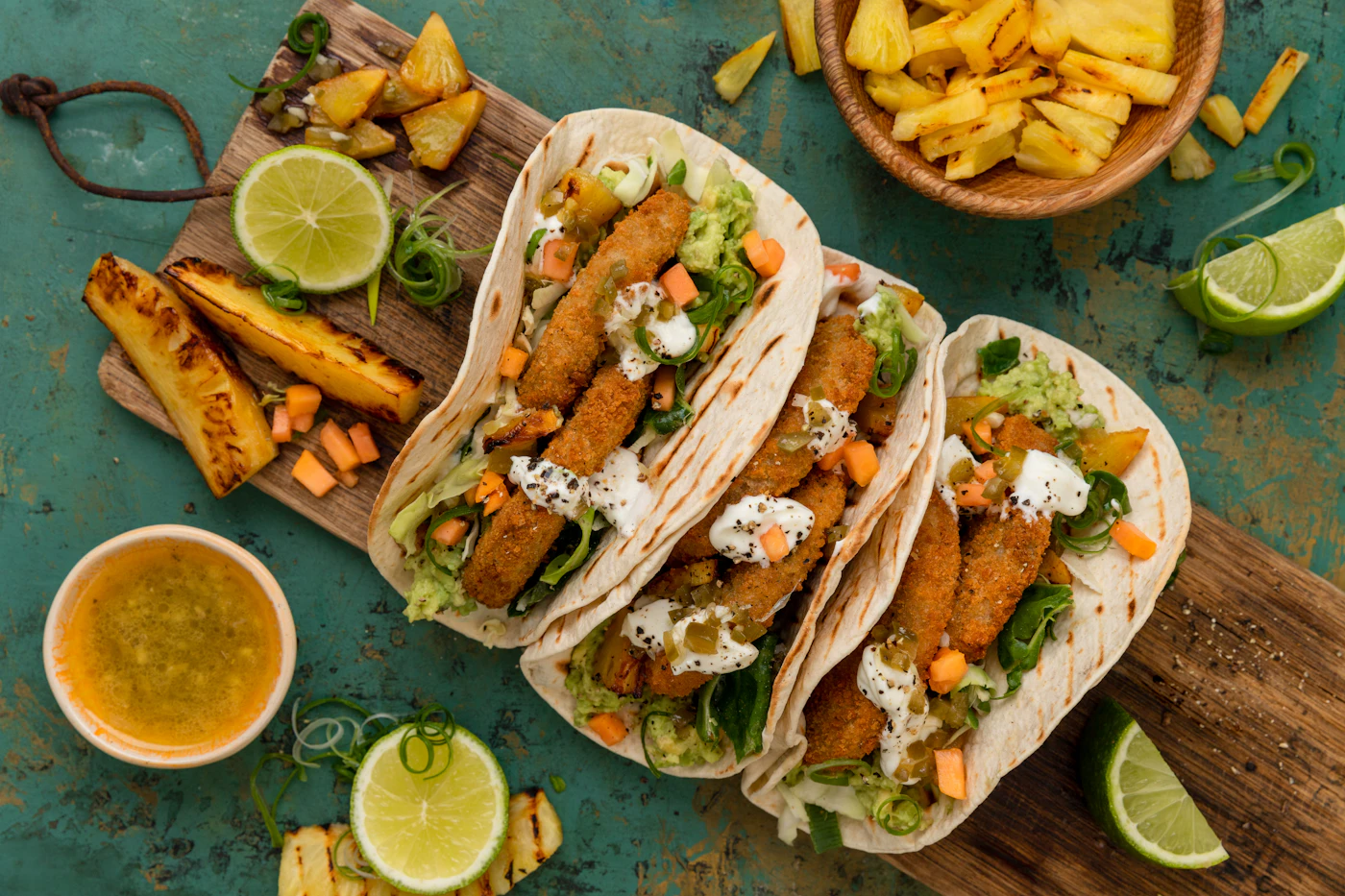 Three crisp fish tacos with pineapple slaw and lime on a serving board