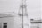 A large telecommunications tower stands next to a modern building. The building has a series of flags on its roof, and part of a patterned flag is visible on the facade. The tower has a complex lattice structure with various antennas attached. The image is in black and white, lending a somewhat industrial and stark appearance.