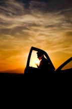 A friendly driver opening the car door for a passenger at sunset.