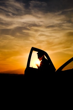 A friendly driver opening the car door for a passenger at sunset.