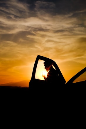 A friendly driver opening car door for a passenger at sunset.