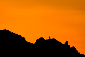 A mountain ridge at twilight with a silhouette of a lone traveler guided by a faint glowing spirit