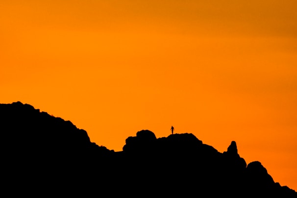 A dramatic portrait of a traveler silhouetted against a fiery sunset on a mountain ridge