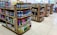 Several shelves are filled with various cleaning products, snacks, and household items. The floor is tiled, and there is ample lighting coming through the store. Each shelf is well-organized with items neatly stacked and price tags visible.
