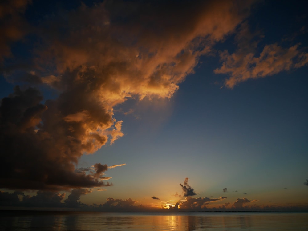 the sun is setting over the ocean with clouds in the sky