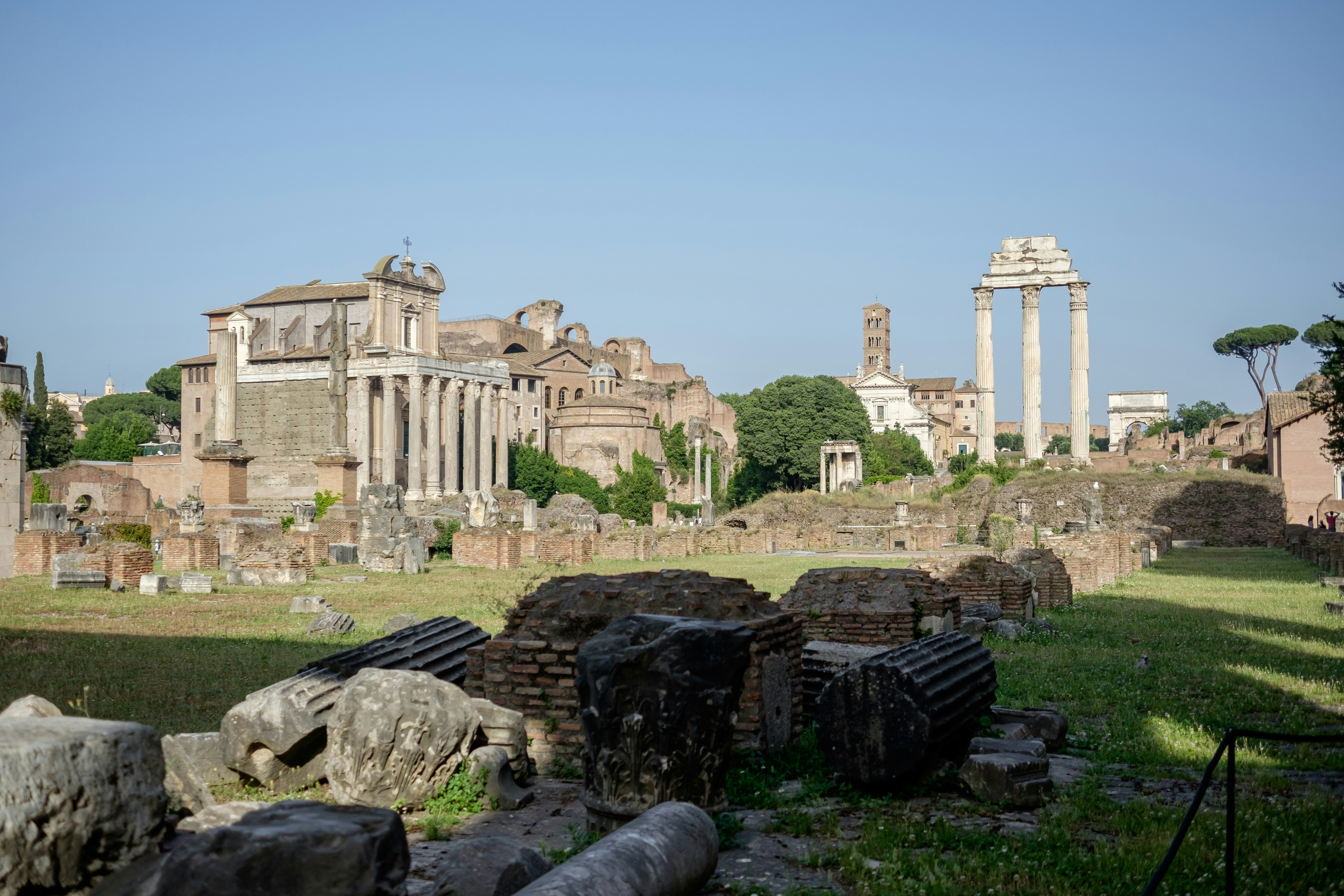 A sunlit view of the Roman Forum ruins with ancient columns and scattered stones.