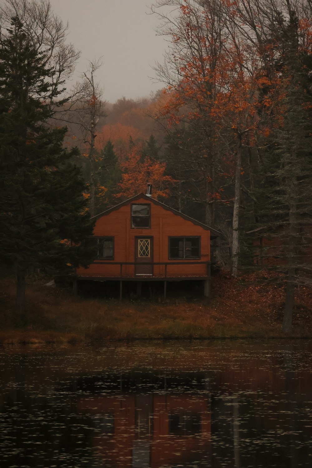 a cabin sits on the shore of a lake surrounded by trees