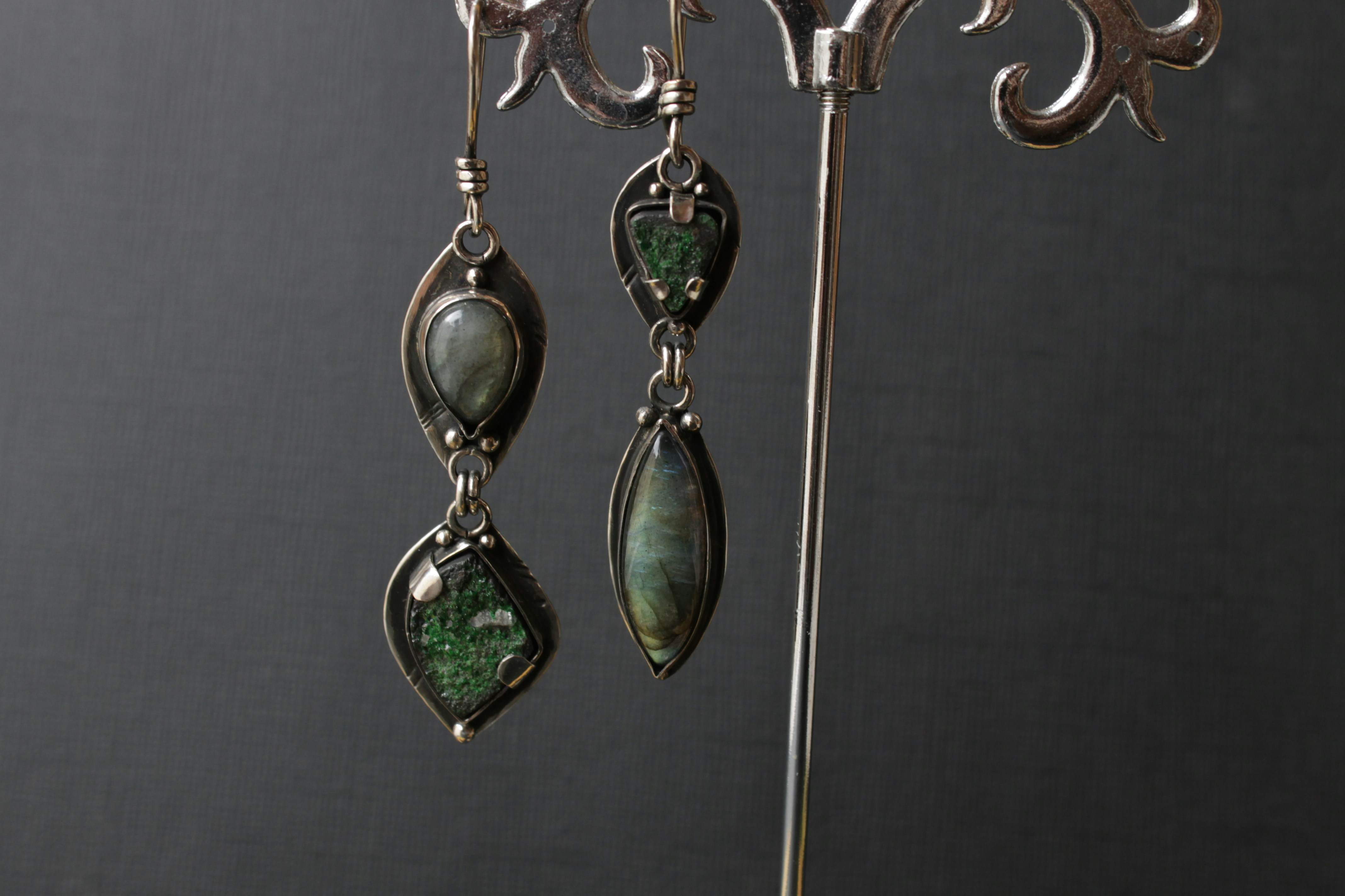 Gold chandelier earrings with emerald stones arranged in cascade pattern, dark background