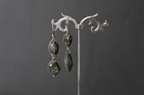 Pair of gold earrings featuring deep green stones, displayed on a dark green silk cloth.