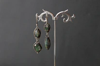 Elegant earrings with sparkling emeralds displayed on a soft velvet cushion.