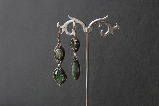 Elegant earrings featuring natural pearls and green tourmaline stones displayed on a hand.