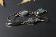 Pair of natural stone earrings with green hues placed on a white marble background.