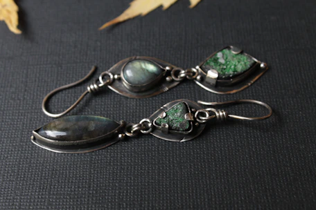 A pair of handcrafted silver earrings featuring vibrant natural gemstones shining under soft light