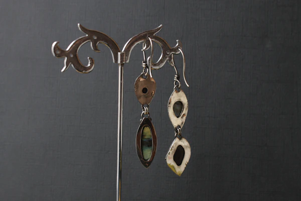 A pair of handcrafted silver earrings with unique geometric shapes against a neutral background.