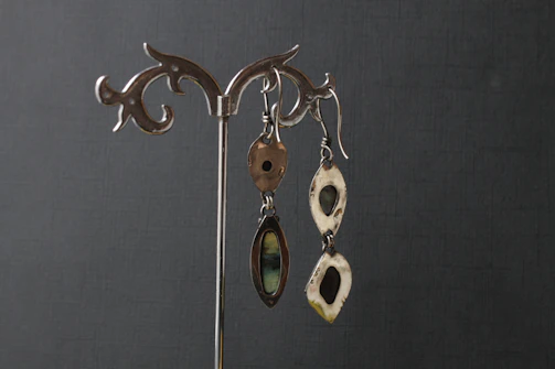 A pair of sharp-edged silver earrings displayed against a neutral metallic background.
