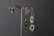 Two pairs of silver earrings with artistic and organic designs hang on a decorative metal stand against a dark textured background. The earrings feature hollow shapes and smooth, reflective surfaces.