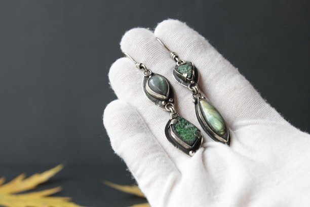 A gentle hand holding elegant porcelain earrings against a muted pastel background.