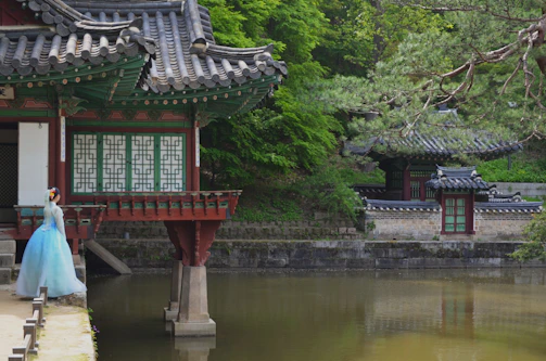 a woman in a blue dress standing in front of a pond