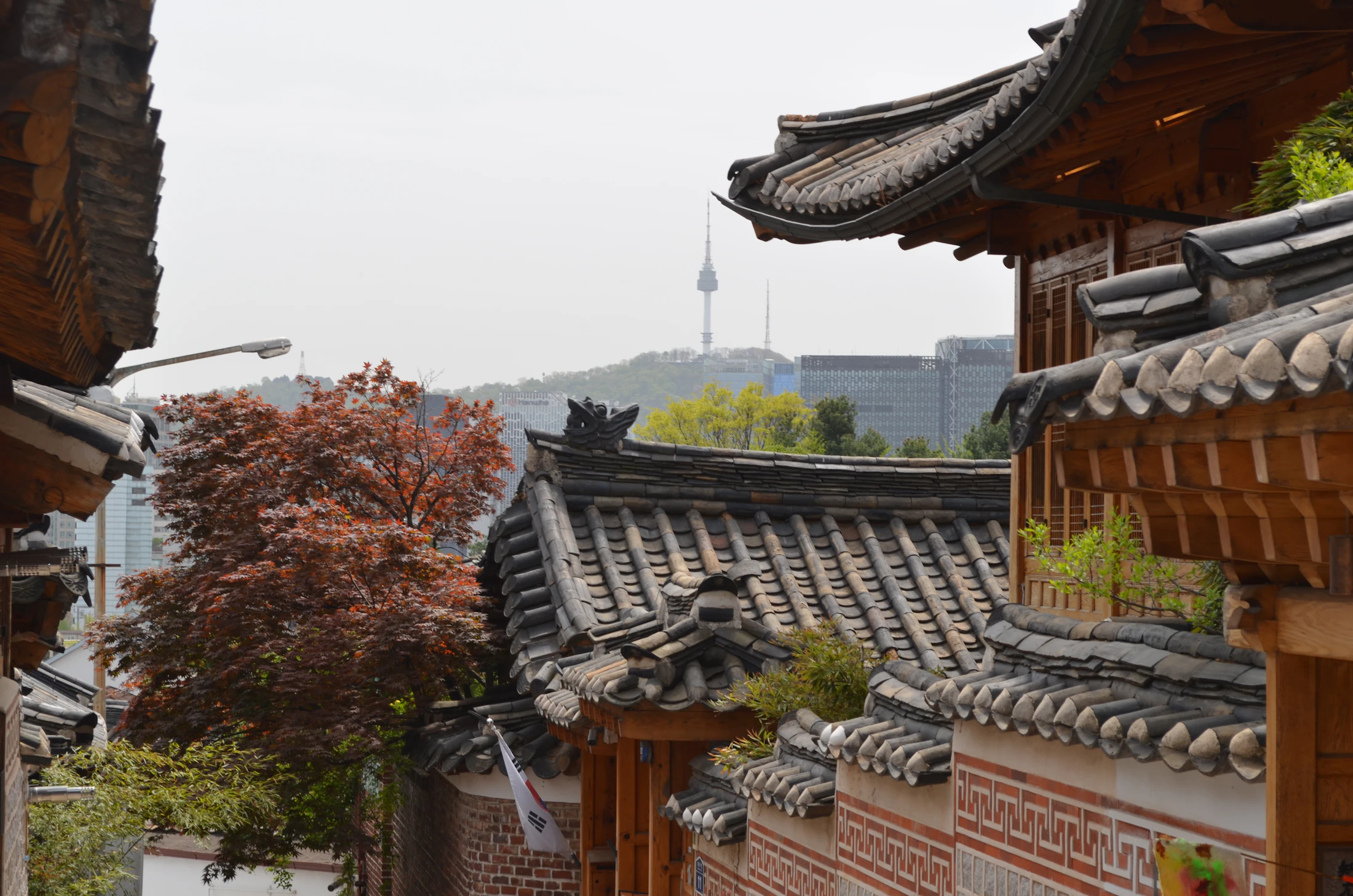 A panoramic view of Bukchon Hanok Village rooftops with the Seoul skyline in the distance