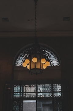Artistic wrought iron chandelier with intricate scrollwork hanging in a cozy room.