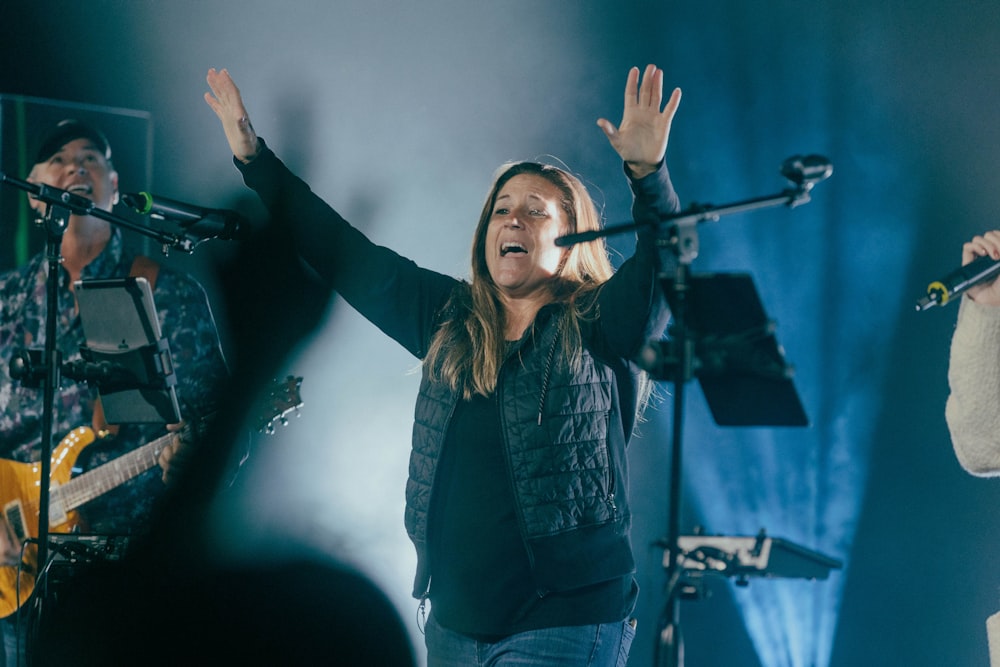 a woman singing into a microphone while holding her hands up