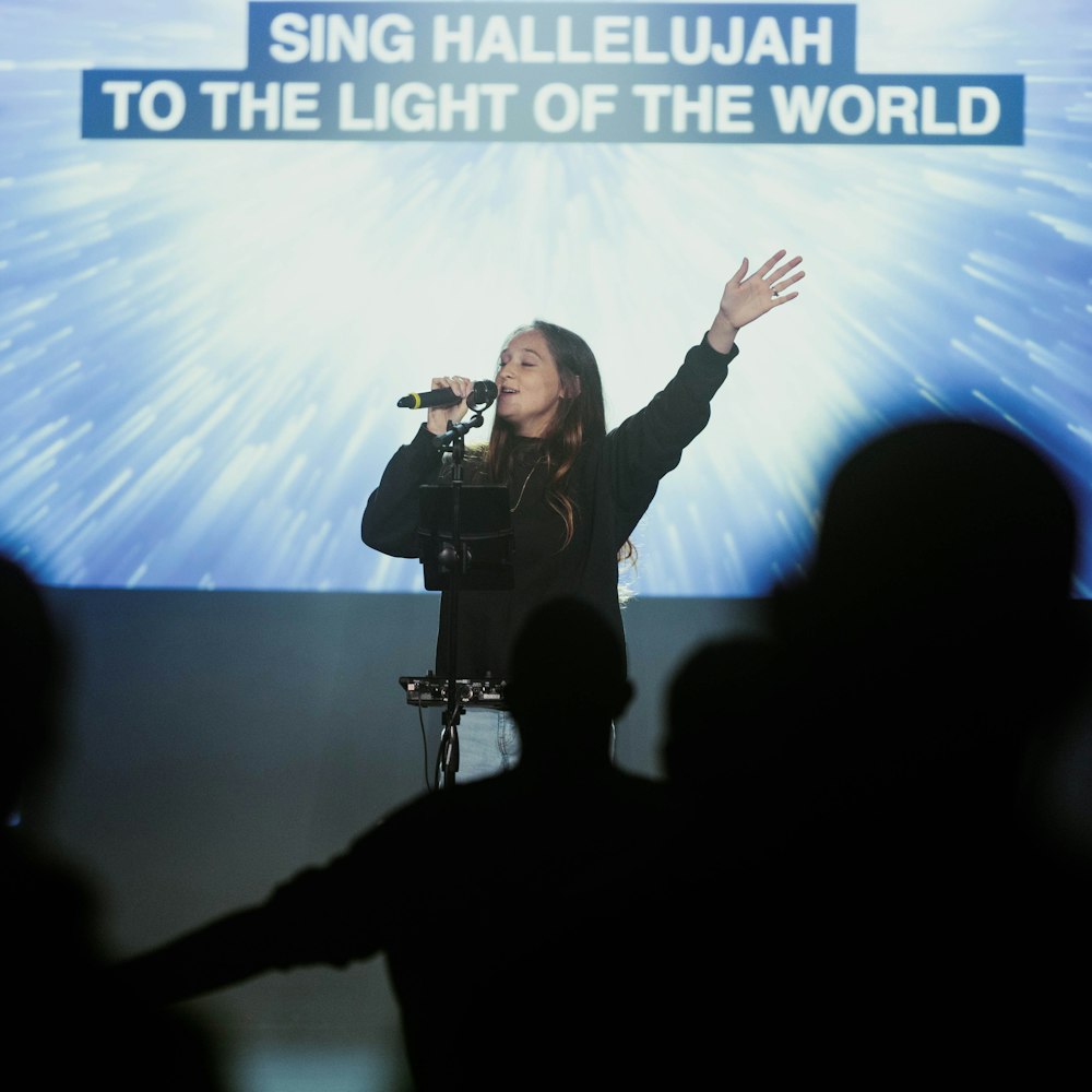 a woman singing into a microphone in front of a large screen