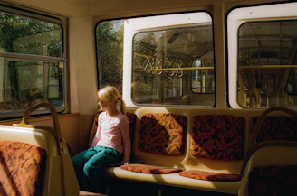 A cheerful child buckled in a bright electric school bus seat, with a parent watching the live tracking app on their phone.