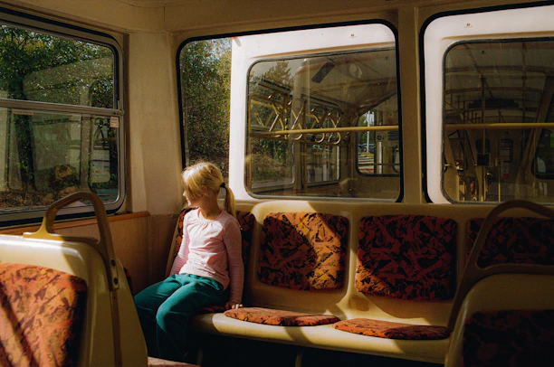 A cheerful child buckled in a bright electric school bus seat, with a parent watching the live tracking app on their phone.