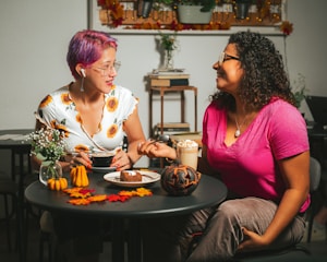 Two women sharing ideas over coffee with soft peachy-pink accents in the background.