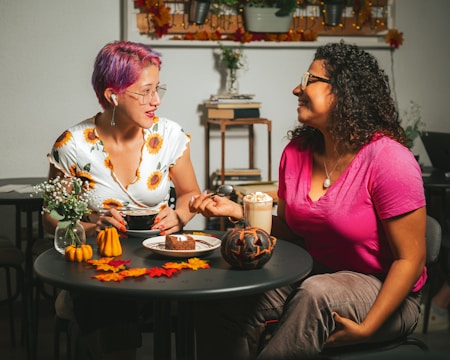 Two women sharing ideas over coffee with soft peachy-pink accents in the background.
