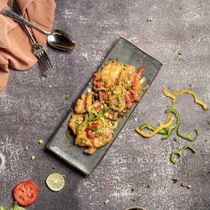 Raw chicken breasts neatly placed on a white plate with red chili peppers.