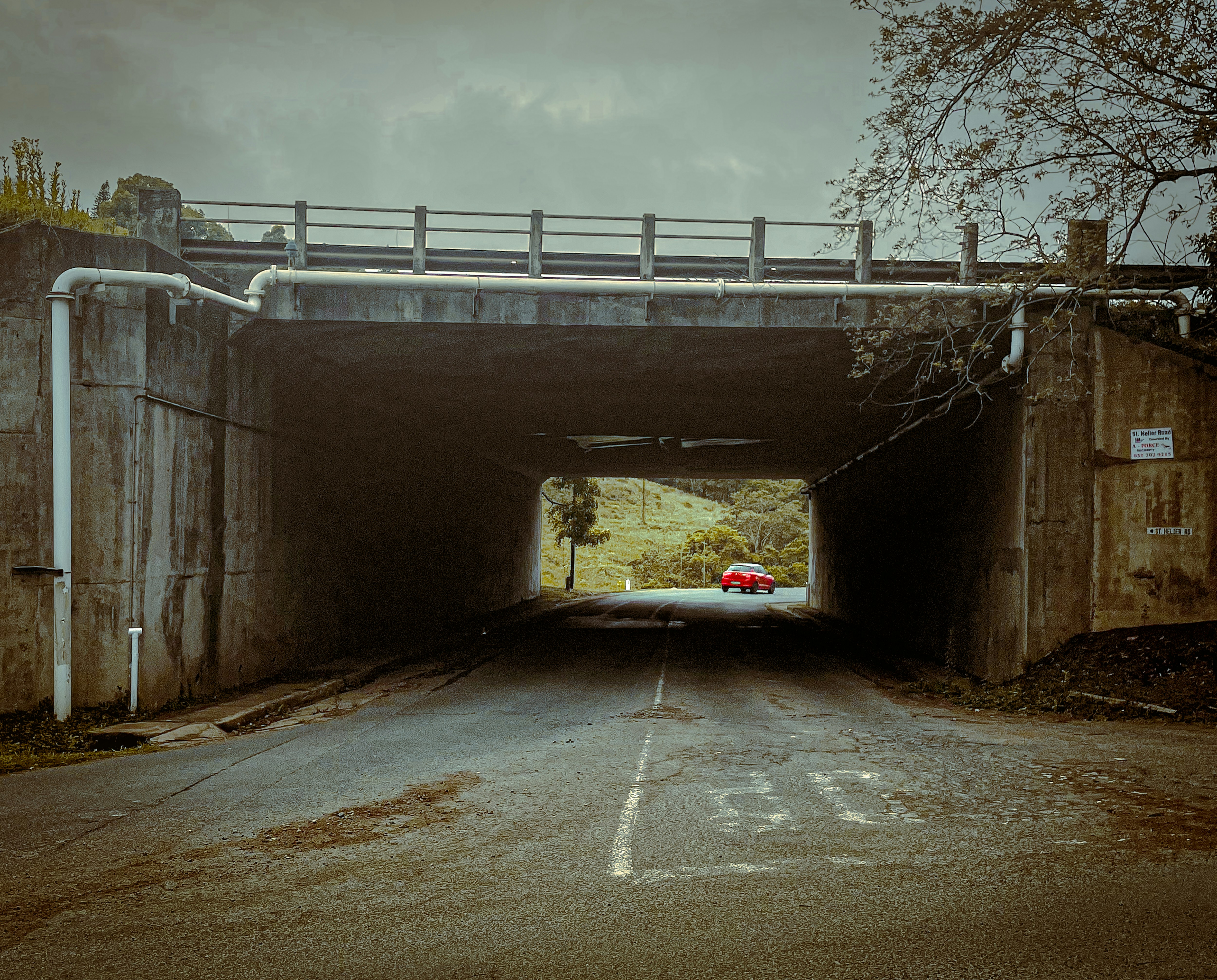 eery photo of a road under a bridge with a car driving off in the distance