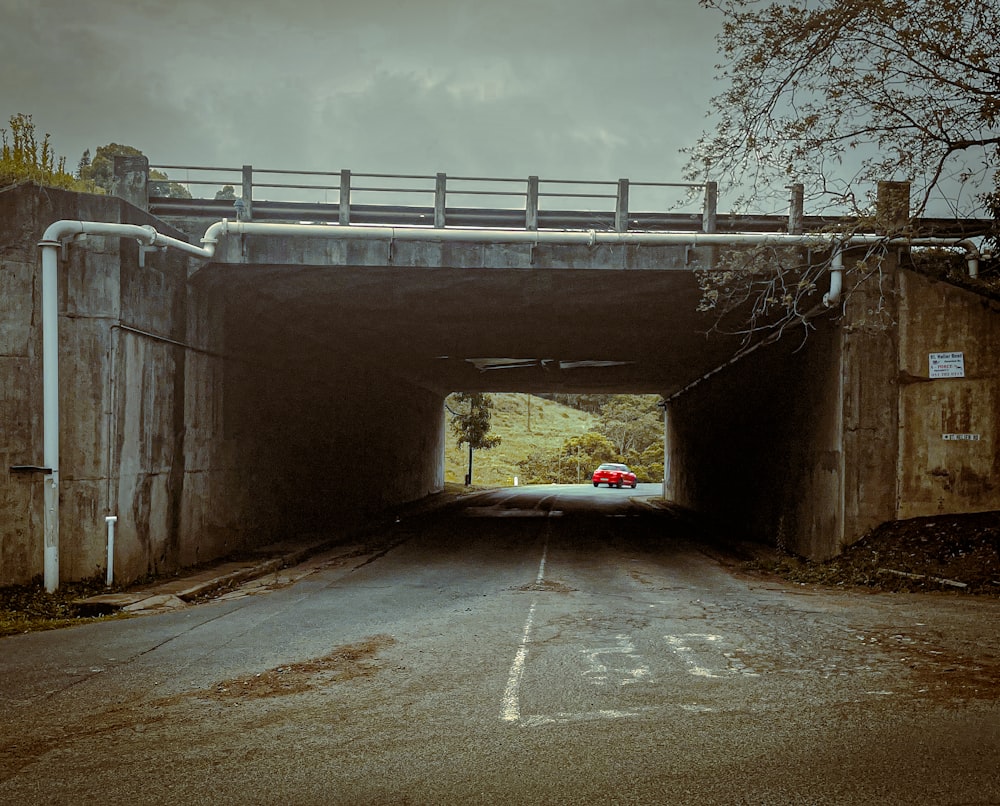 a red car driving through a tunnel under a bridge