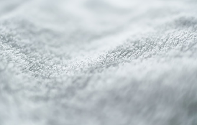 A close-up view of a textured white fabric with small loops, likely a towel or similar material. The texture appears soft and slightly uneven.