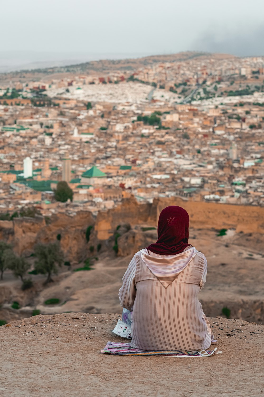 eine Person, die auf einem Hügel mit Blick auf eine Stadt sitzt