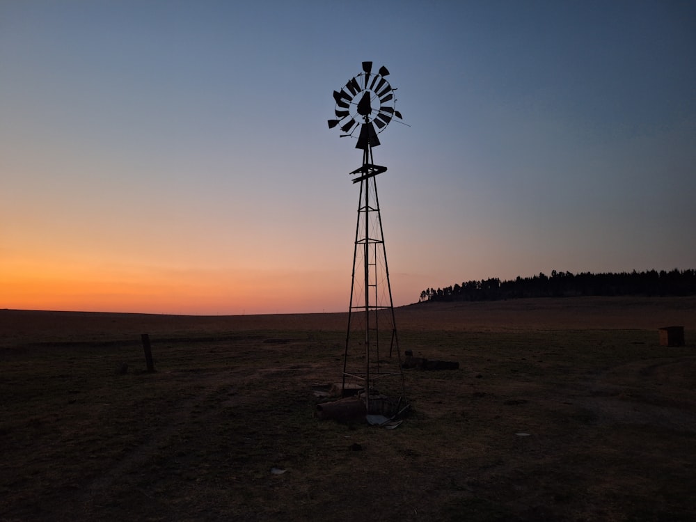 a windmill in the middle of a field at sunset