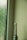 An electric toothbrush stands upright beside a textured glass window with water droplets. The setting appears to be minimalistic, with a light green wall and a faintly lit ambiance.