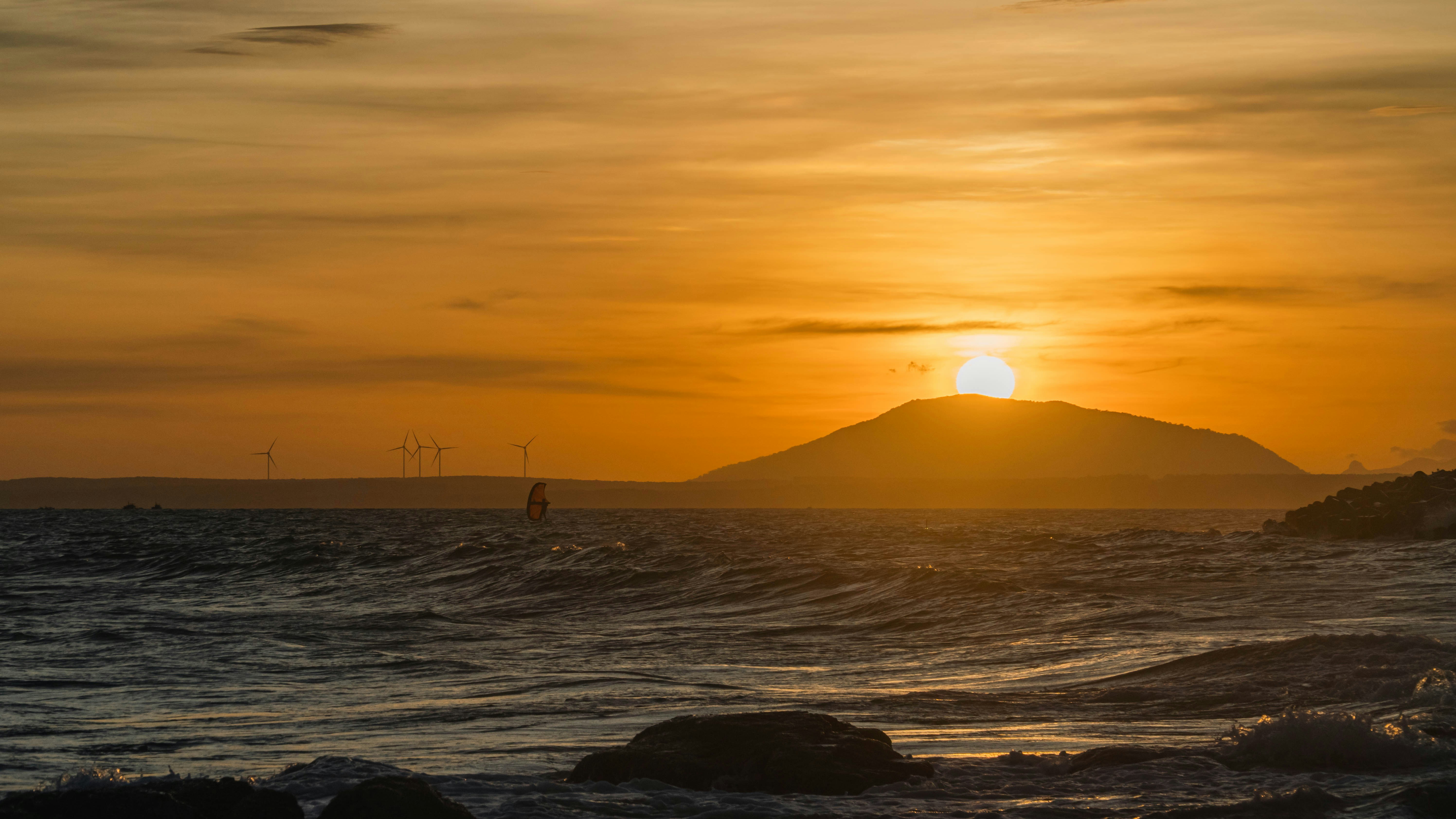 the sun is setting over the ocean with a small island in the distance
