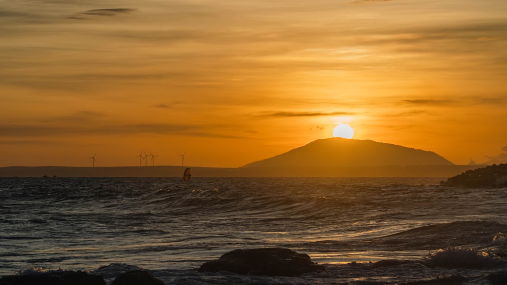 the sun is setting over the ocean with a small island in the distance