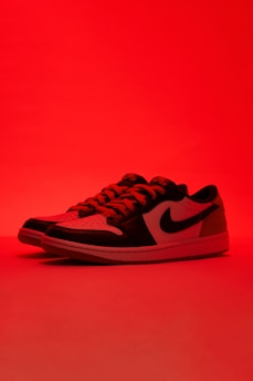 A pair of low-top sneakers with black and white leather panels is illuminated by a red light. The sneakers have a black swoosh logo on the side and are presented against a solid red background, giving a dramatic and bold appearance.