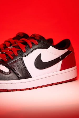 A stylish sneaker featuring a combination of black, white, and red leather with red laces against a vibrant red background. The iconic swoosh logo is prominently displayed on the side.