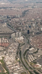 An aerial view of a densely populated urban area with numerous high-rise buildings and residential complexes. Major highways with visible traffic flows cut through the cityscape, connecting different parts of the metropolis. The area appears to be a mix of commercial and residential districts, with varying building densities.