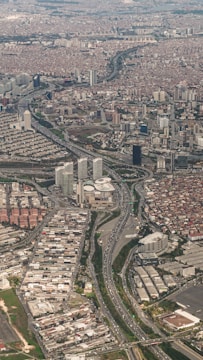 An aerial view of a densely populated urban area with numerous high-rise buildings and residential complexes. Major highways with visible traffic flows cut through the cityscape, connecting different parts of the metropolis. The area appears to be a mix of commercial and residential districts, with varying building densities.