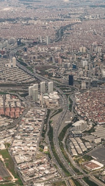 An aerial view of a densely populated urban area with numerous high-rise buildings and residential complexes. Major highways with visible traffic flows cut through the cityscape, connecting different parts of the metropolis. The area appears to be a mix of commercial and residential districts, with varying building densities.
