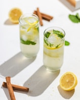 Refreshing cold drinks in tall glasses with ice and lemon slices on a wooden table.