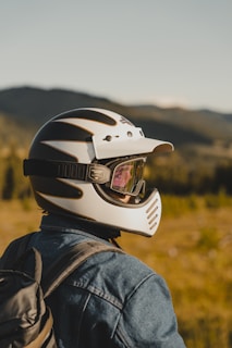 A portrait of a smiling person geared up in motorcycle safety apparel against a backdrop of winding roads.