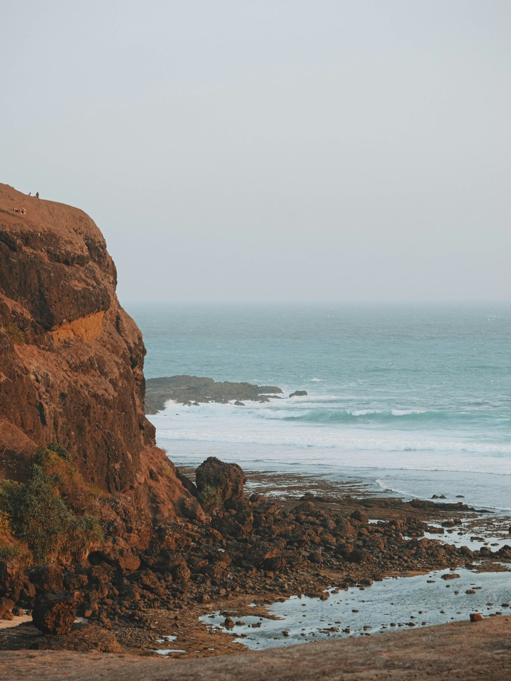 a couple of people standing on top of a cliff near the ocean